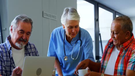 Nurse-serving-cup-of-tea-while-senior-friends-using-laptop-4k