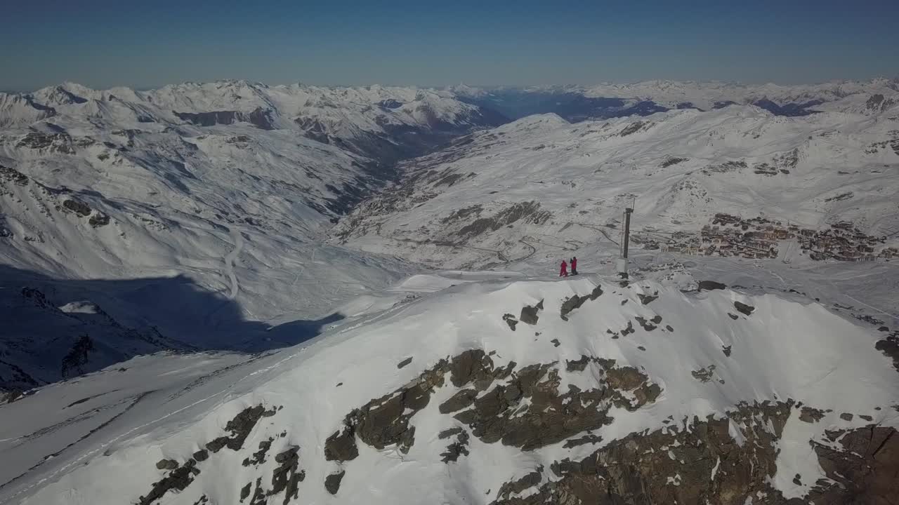 adelantamiento aéreo de dos esquiadores en la cima de un pico de montaña revelando un amplio paisaje de valle cubierto de nieve - toma amplia del dron