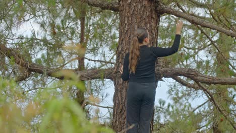 woman in black tracksuit gently touching pine tree with her hands, static