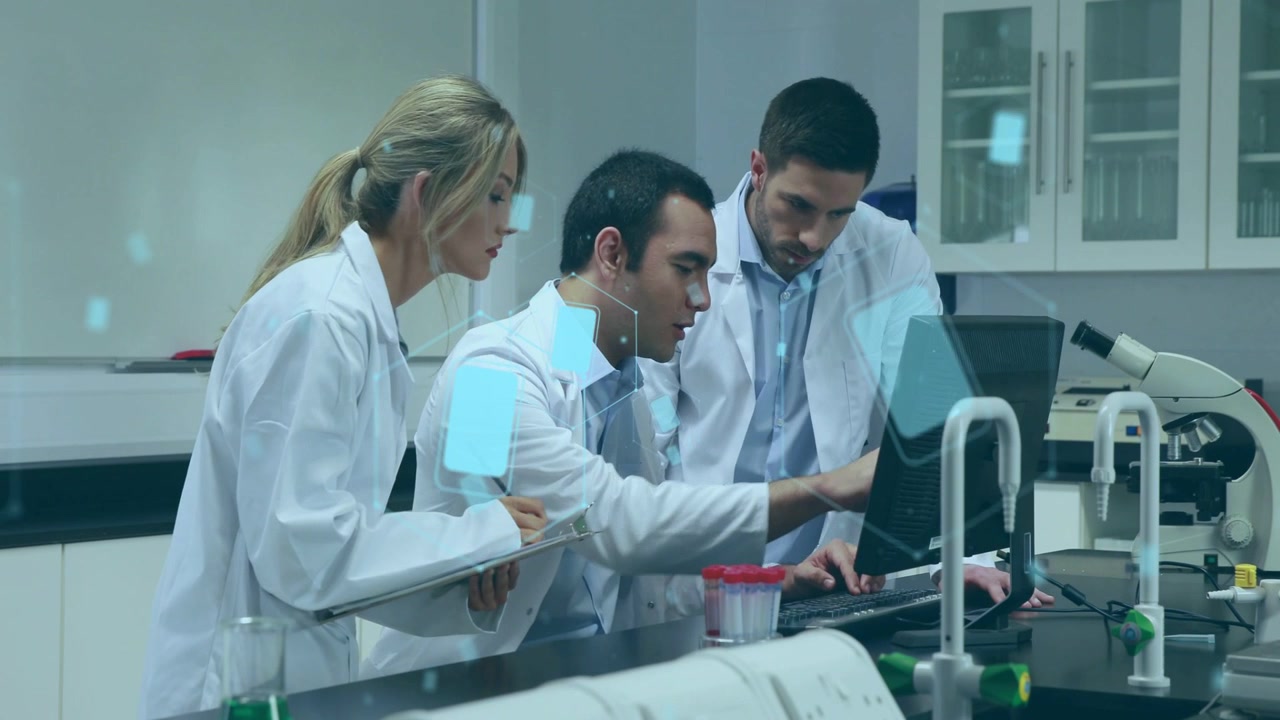 Científico principal inclinado hacia adelante y señalando el monitor, el equipo del laboratorio acercándose para revisar datos