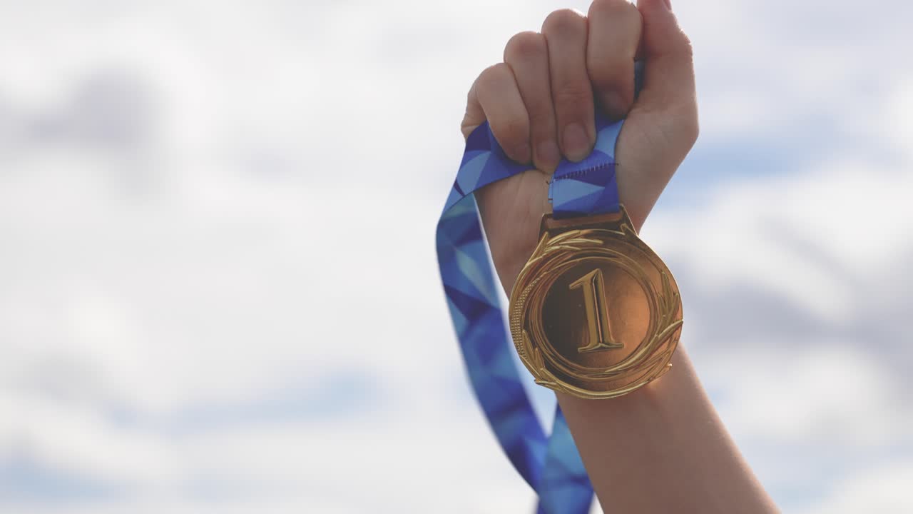 Close-up of a raised hand holding a medal against the sky. Represents achievement, success, victory, and recognition. Ideal for motivation, competition, and award concepts