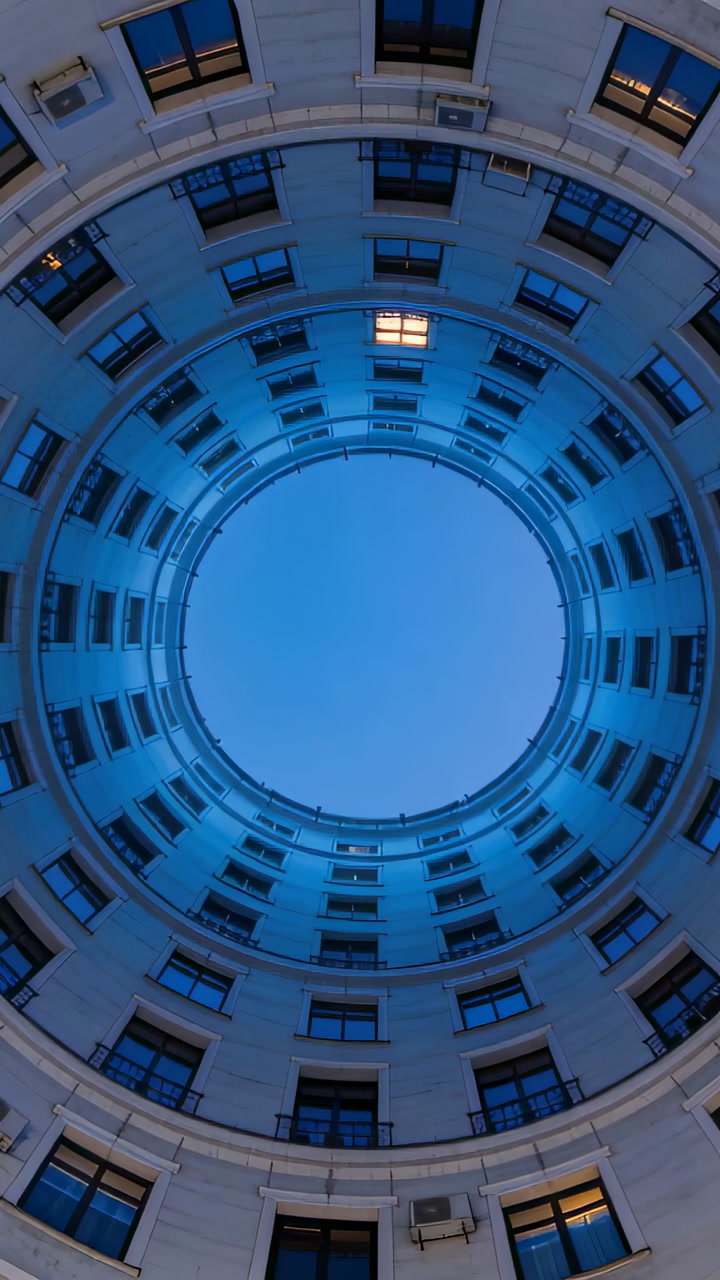 Vertical video: Tilting camera framing central circular atrium at twilight, revealing lit windows