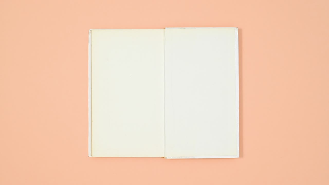 White hardcover book appear from wrapped paper and open on orange theme. Stop motion flat lay