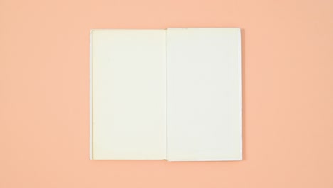 white hardcover book appear from wrapped paper and open on orange theme. stop motion flat lay