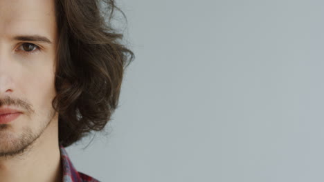 close up of the half male face with long hair looking in the camera and then smiling on the white wall background