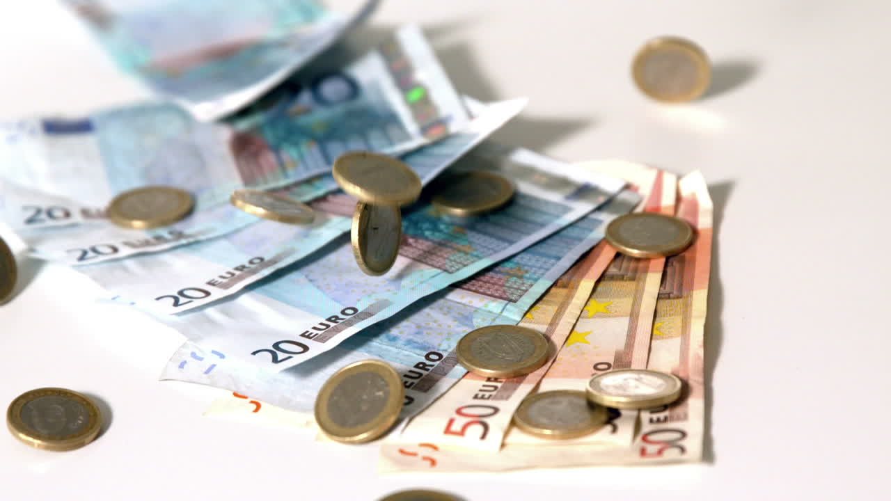Eurosedler og mynter faller på hvit overflate