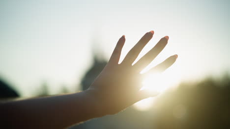 close up of hand reaching towards sunlight, creating beautiful interplay between fingers and sun rays, with blurred background emphasizing serene outdoor setting