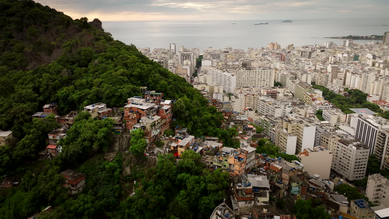 Aerial drone view of social inequality in Rio de Janeiro, dense favela on lush green hill contrasts with modern buildings of Copacabana. Brazil