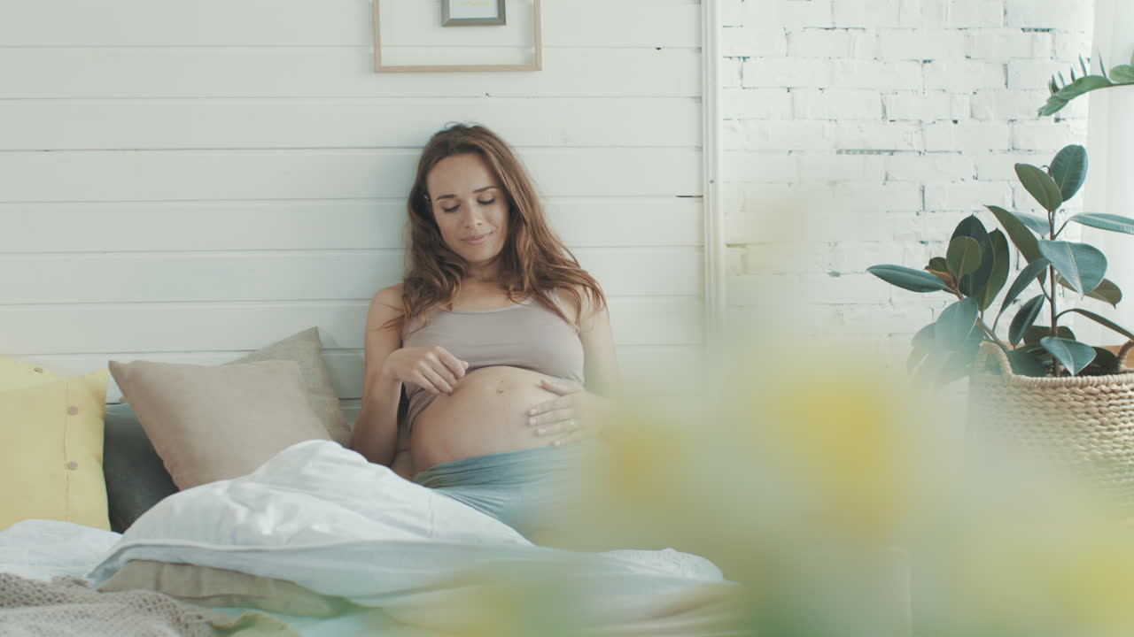 будущая мать чувствует боль при беременности дома. напряженный живот. мать сидит в постели.