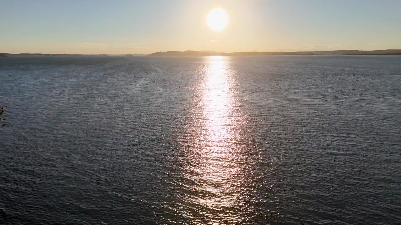 Aerial view of bright sun reflecting on shimmering sea at sunset in Nelson Bay, Australia.