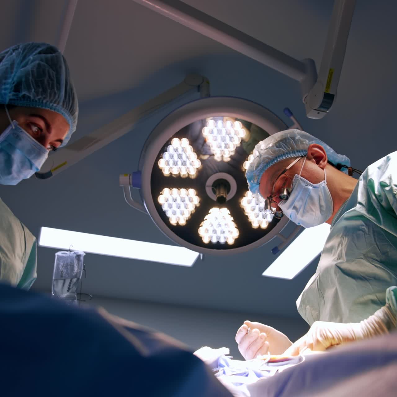 Un médico con gafas especiales trabaja cuidadosamente con herramientas metálicas. Una enfermera le ayuda y le pasa las herramientas a un cirujano. Vista en ángulo inferior