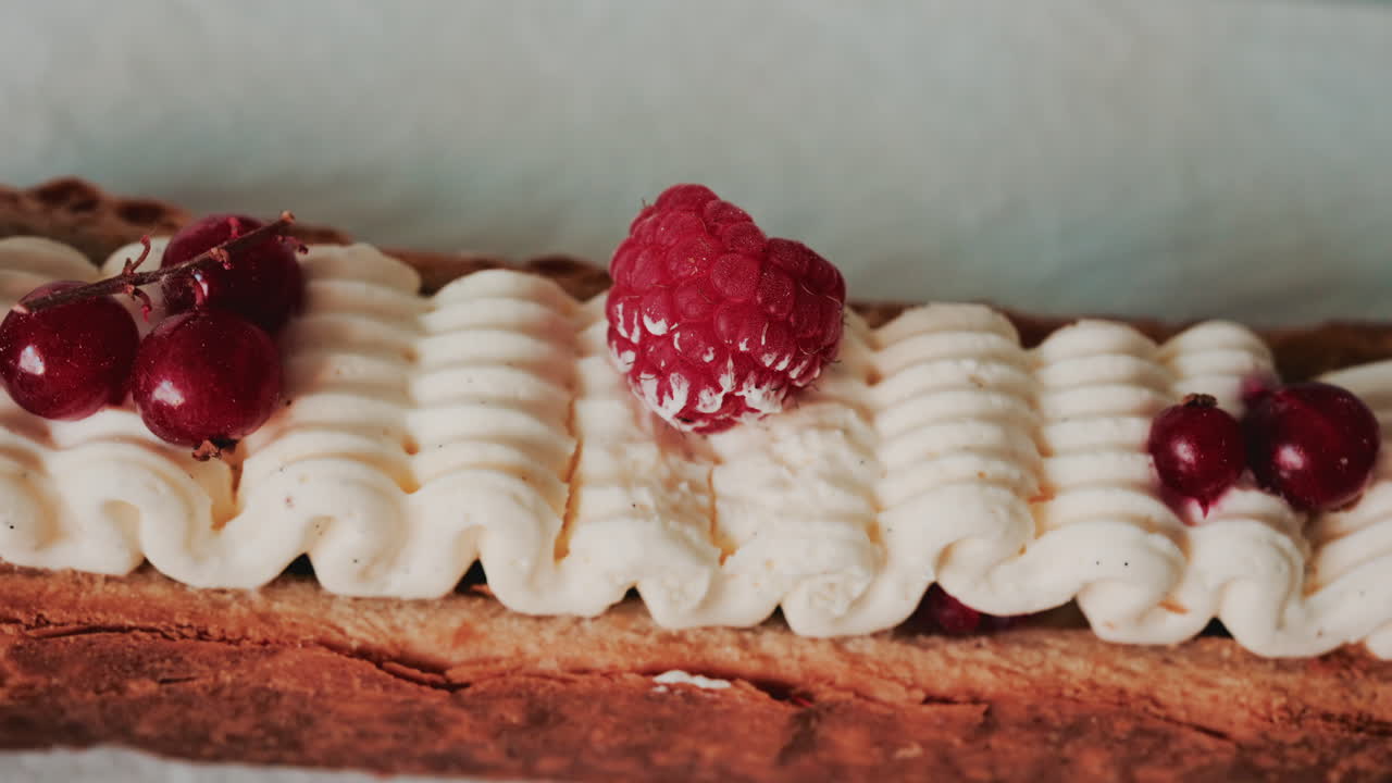 Close up of a gourmet pastry topped with cream, raspberries, and red currants