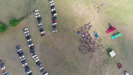 toma de arriba hacia abajo de la multitud reunida para un bautismo con autos estacionados en el campo