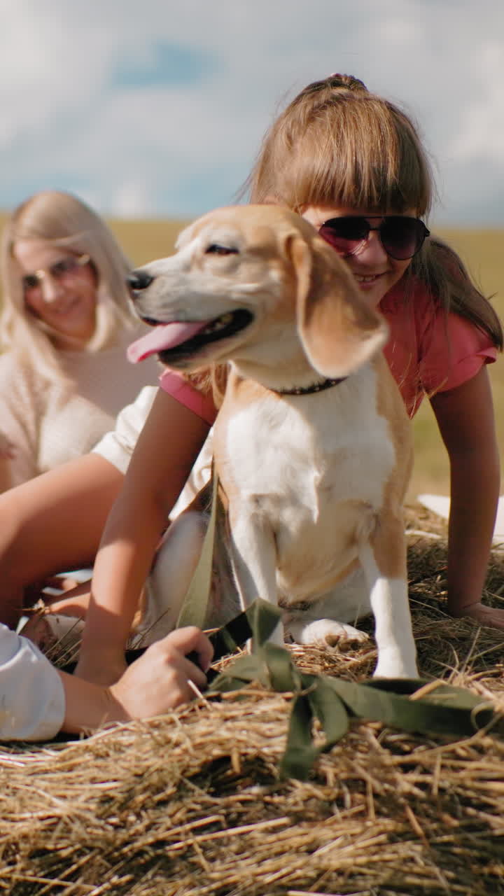 어린 소녀는 줄을 고 개와 함께 건조한 에 올라, 혀를 꺼내, 여자가 아이를 도와주는 동안, 다른 여자는 빛의 시골에서 근처에 서 있으며, 굴곡 된 과 멀리 나무가 있습니다.