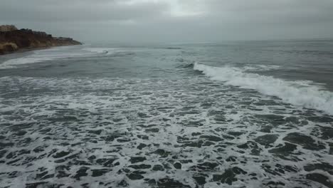 low view from a drone flying over the coast to the sea showing the waves and the landscape
