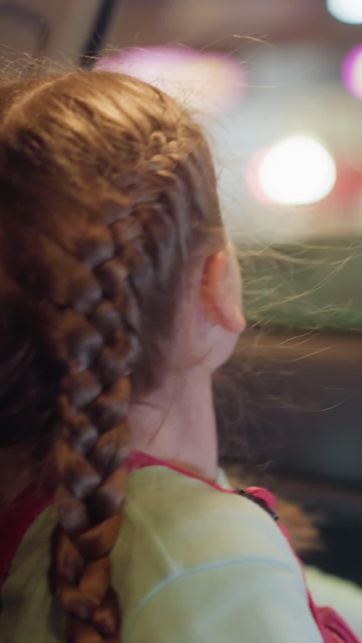 una vista de cerca de un niño enrollando el vidrio del coche, con una vista borrosa de las luces a través de la carretera y pasando por los coches, el niño tiene el cabello trenzado