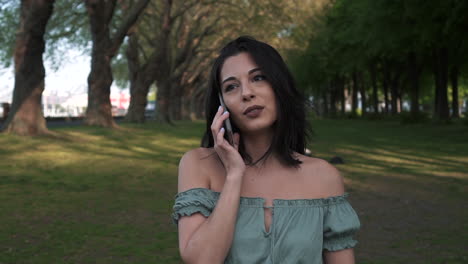 portrait of smiling woman using smartphone to make a call while walking in a beautiful park in london