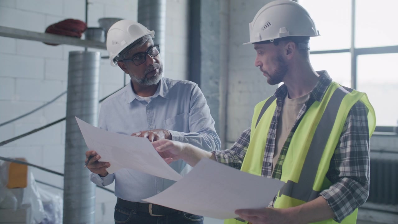 Senior Engineer and Contractor Discussing Floor Plans on Construction Site