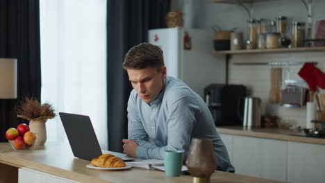 frustrated business man feeling stressed looking at laptop screen on kitchen.