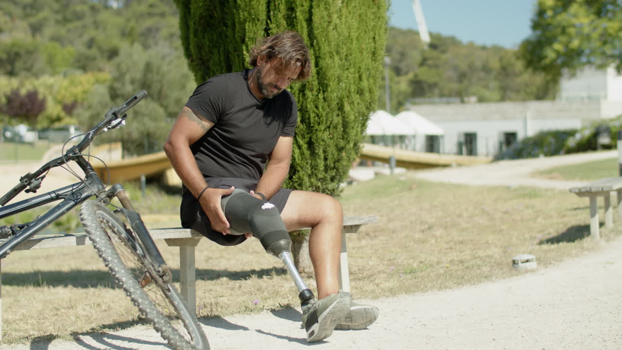 Long shot of sportsman fixing prosthesis of leg before cycling