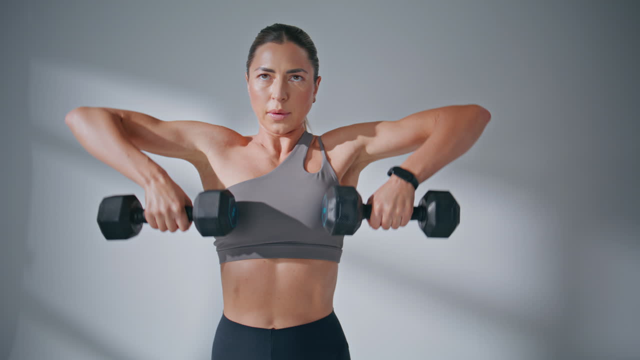 Tensed athlete exercising dumbbells in studio closeup. Woman lifting equipment