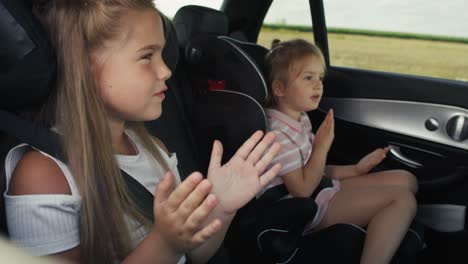 Two-caucasian-female-children-riding-in-the-car-in-the-back-seat-and-singing.