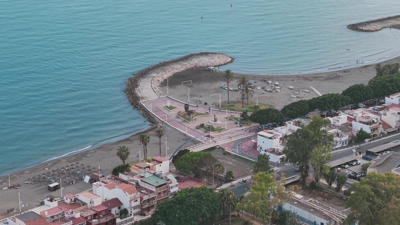 Frangiflutti curvi, spiaggia sabbiosa e lungomare mediterraneo creano una vista costiera panoramica di Malaga dall'alto