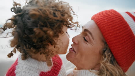 happy child kissing mom having fun together at ocean shore together closeup.