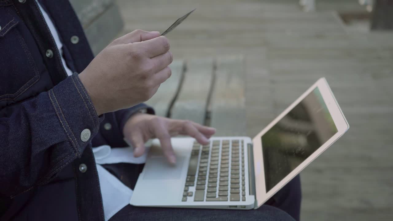 hombre enfocado con tarjeta de crédito usando portátil al aire libre