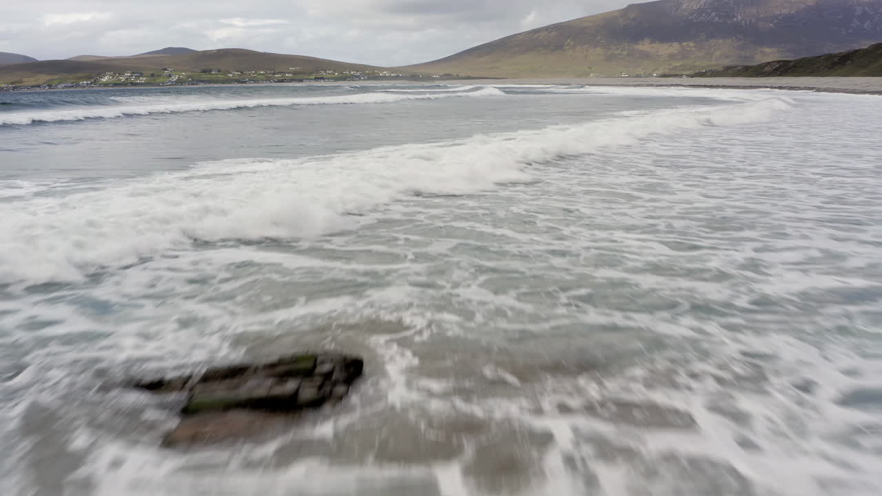Crashing waves spread white water froth along open ocean, aerial dolly, slow motion