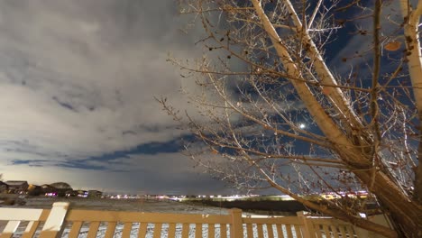 lapso de tiempo nocturno de nubes, la luna poniente, estrellas giratorias y senderos de aviones en el cielo invernal sobre un suburbio urbano