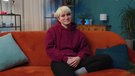 a young blonde woman sitting on a couch and smiling at the camera