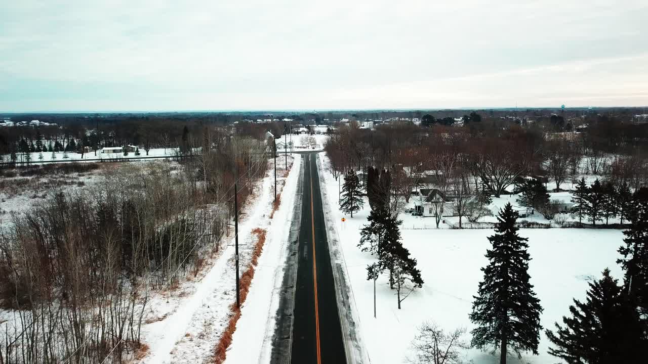 Aerial shot following desolate road through snowy farmland. 4K