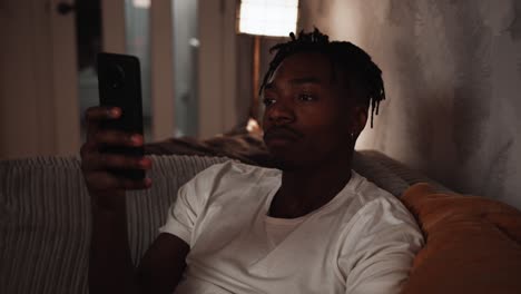 young black male sitting on the sofa at home using a smart phone