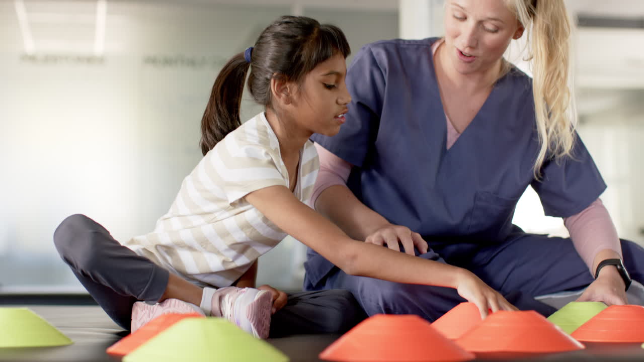 Playing with colorful cones, girl with cerebral palsy in rehabilitation focusing with therapist