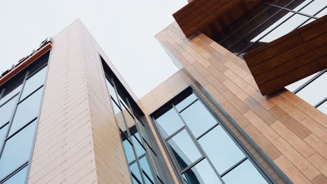 upward angle view of modern fitness building featuring large glass windows and wooden panel facade under bright daylight sky, showcasing sleek architecture and vertical lines in urban setting