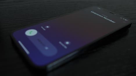 close-up shot of an iphone receiving a call from an unknown number on black wooden table