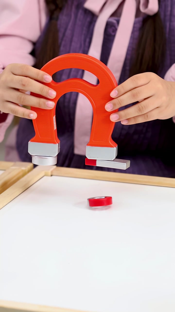Primer plano de un estudiante usando un imán grande de herradura para atraer pequeños objetos metálicos
