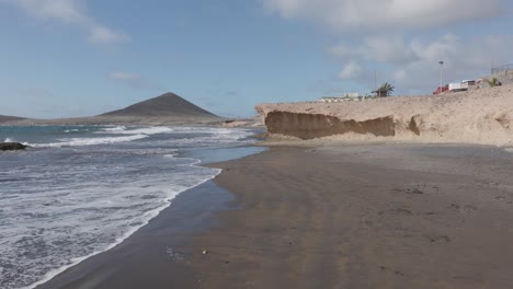 pov view of rock formations on a beach and the ocean during a sunny day in el médano, tenerife, canary islands, spain.
