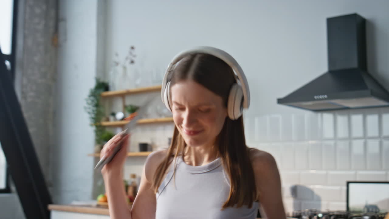 Singing woman chopping vegetables in headphones at domestic kitchen closeup
