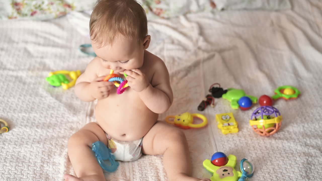 Caucasian blonde baby boy on a bed, playing with toys