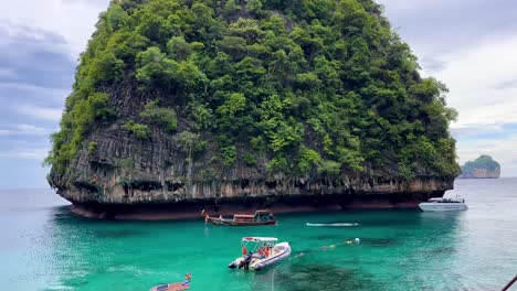 a captivating panorama of the forested rock formation at the entrance to maya bay, thailand, with two boats sailing, and the water displaying a deep green hue, creating a mystical atmosphere