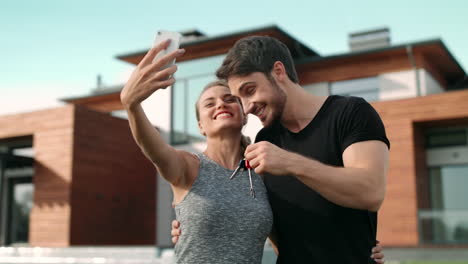 una pareja feliz tomando una foto selfie con las llaves de la casa fuera de la residencia.