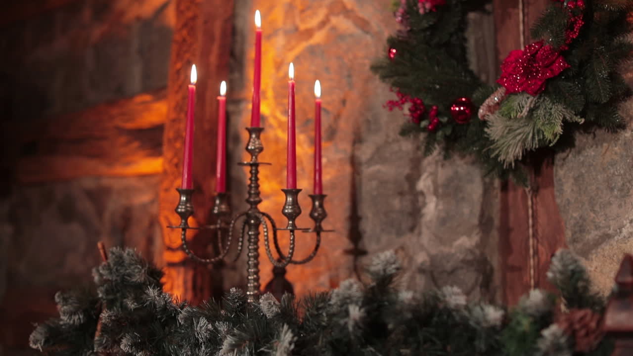 Christmas wreath with red flowers and berries hanging on the stone wall. Red burning candles on the silver candlestick.