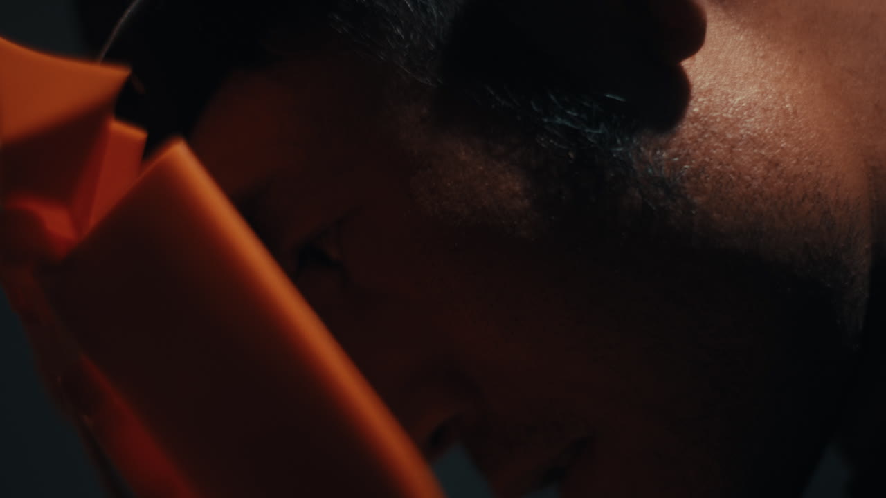 Close up of mechanic with sweat on brow under workshop light wearing mask, slow motion