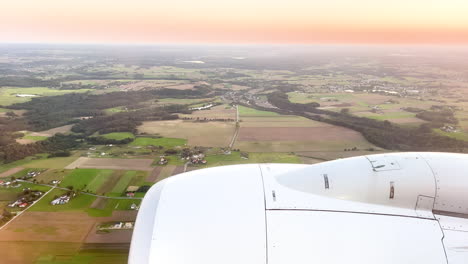 Golden sunset from an airplane window, with the aircraft&#039;s engine over a pastoral landscape