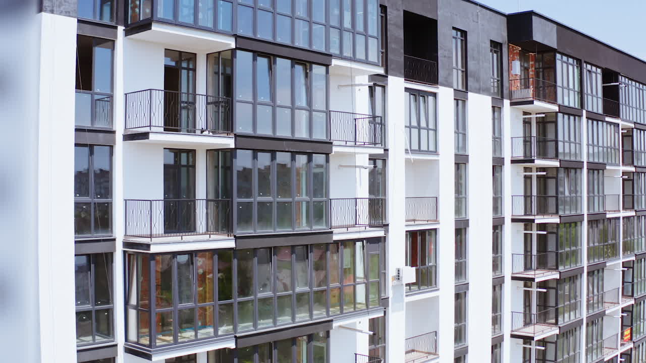 Beautiful new housing apartments. Modern facade of a high-rise building with a cityscape reflection in windows. Multi-storey building in white and black colors. Front view.
