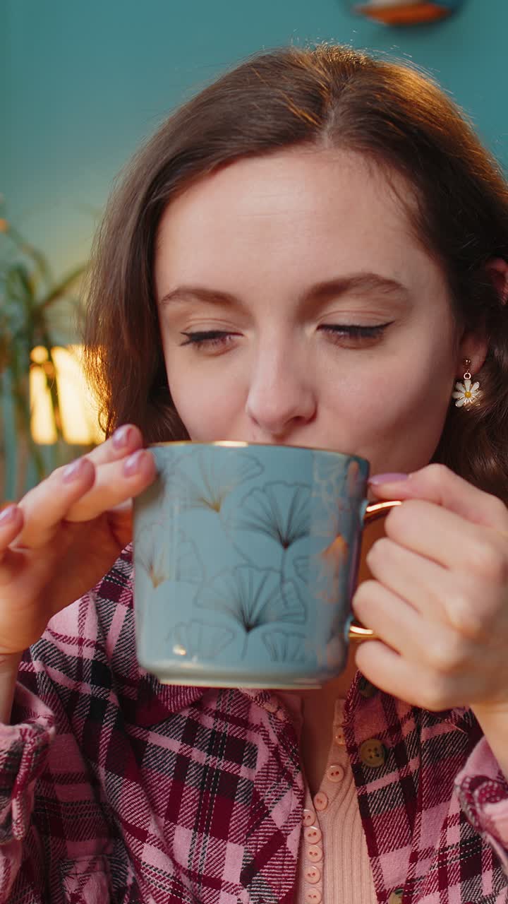 노트북 컴퓨터에서 일하는 사업가 여성이 뜨거운 커피 한 잔을 마시며 집 사무실에서 테이블에 앉아 있습니다.