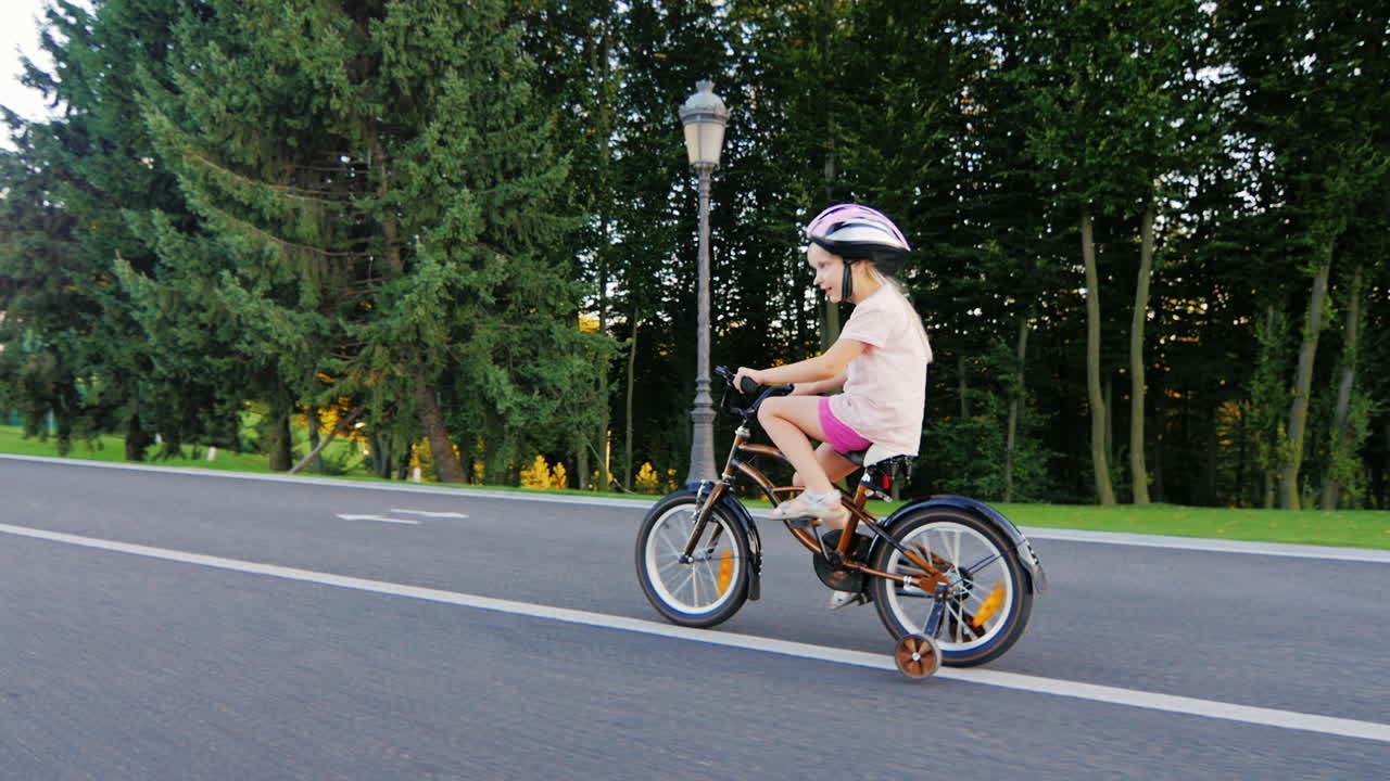 여분의 바퀴가 웃고 있는 자전거를 타는 5살짜리 재미있는 소녀