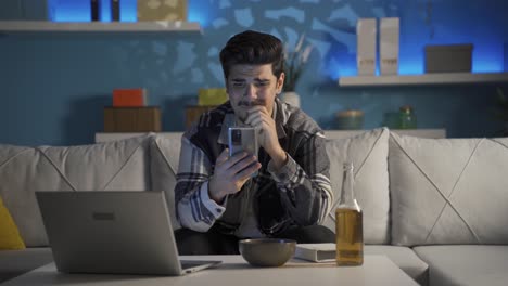 joven llorando y enviando mensajes de texto por teléfono bebiendo alcohol.